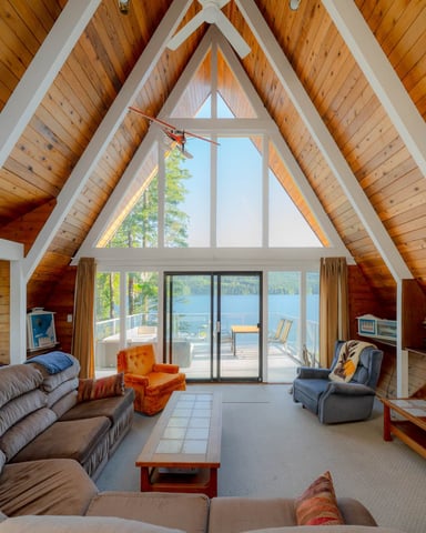 Vaulted wood cabin living room with white beams, large windows, lake view, and glass doors to deck