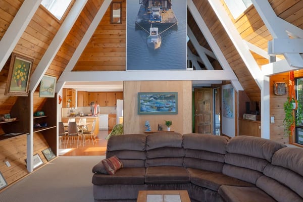 Lakefront deck with glass railings, lounge chairs, and mountain views surrounded by tall pine trees