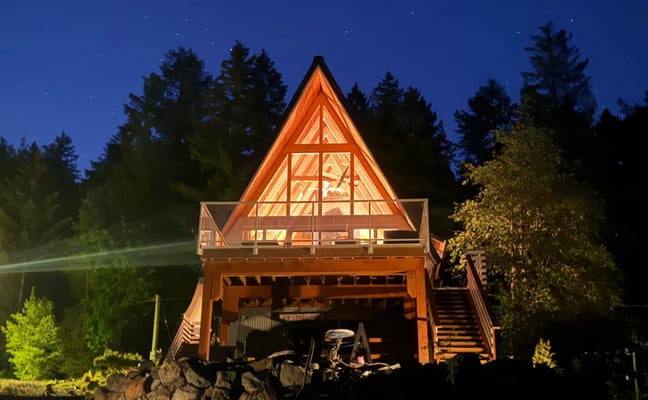Waterfront cabin surrounded by golden larch trees with dock, yellow umbrella, and boats on lake
